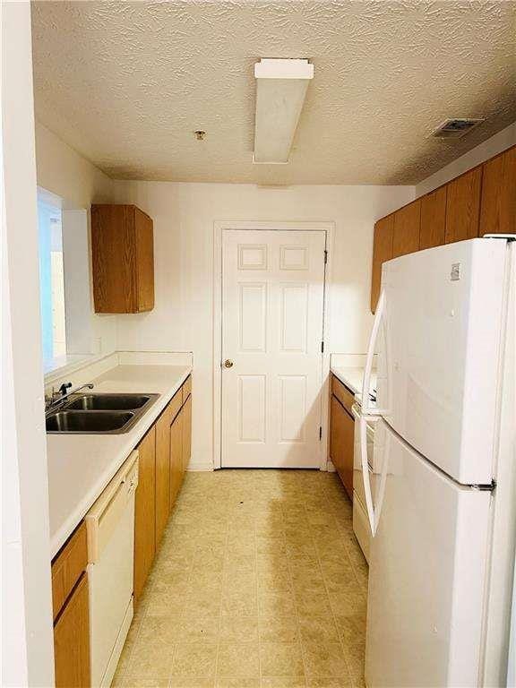 kitchen with white appliances, brown cabinetry, light countertops, and a sink