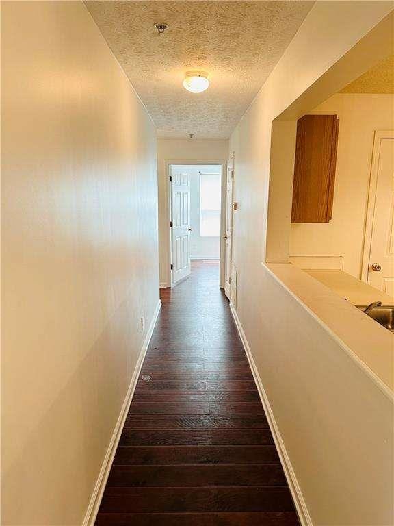 corridor with baseboards, dark wood-type flooring, and a textured ceiling