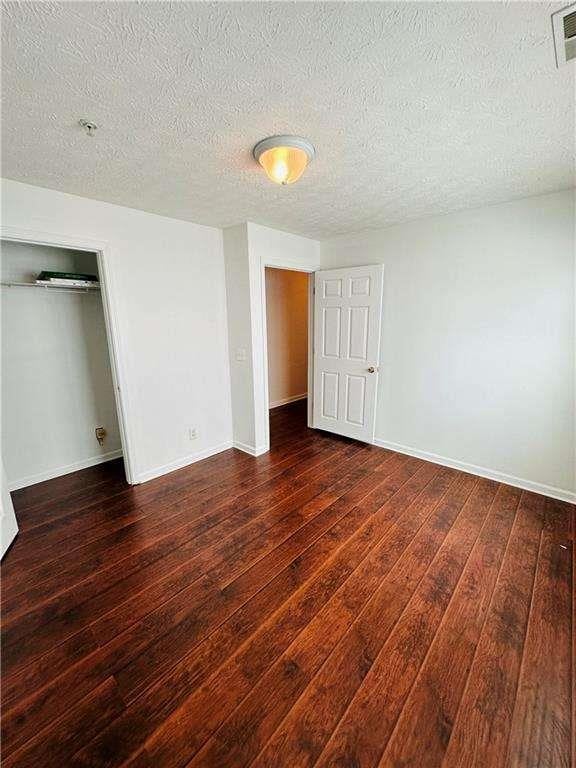 unfurnished bedroom featuring hardwood / wood-style floors, visible vents, baseboards, a closet, and a textured ceiling