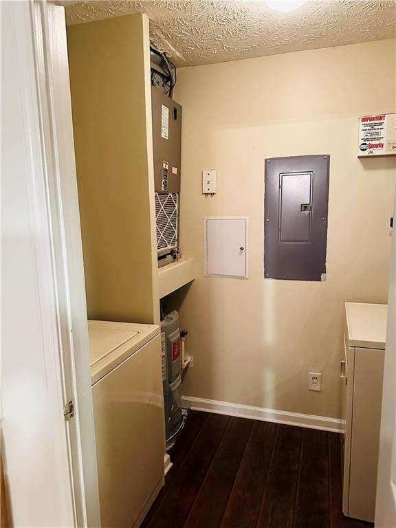 washroom featuring baseboards, electric panel, laundry area, a textured ceiling, and dark wood-style flooring