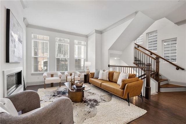 living area featuring baseboards, wood finished floors, a glass covered fireplace, and ornamental molding