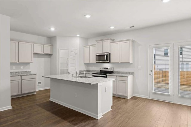 kitchen with light stone countertops, sink, dark wood-type flooring, a kitchen island with sink, and appliances with stainless steel finishes