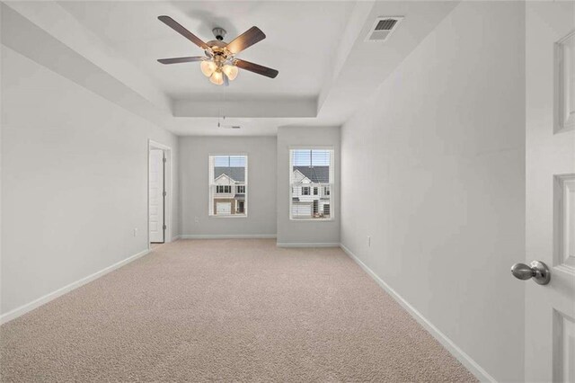 carpeted spare room with a raised ceiling and ceiling fan