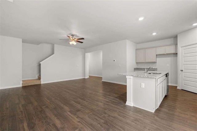 kitchen with a center island with sink, sink, dark hardwood / wood-style floors, ceiling fan, and light stone countertops