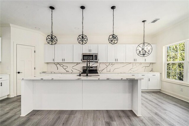 kitchen with light stone countertops, light wood-type flooring, stainless steel appliances, a center island with sink, and white cabinetry