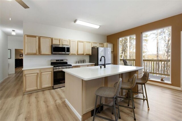 kitchen with ceiling fan, a kitchen breakfast bar, light hardwood / wood-style flooring, a kitchen island with sink, and appliances with stainless steel finishes