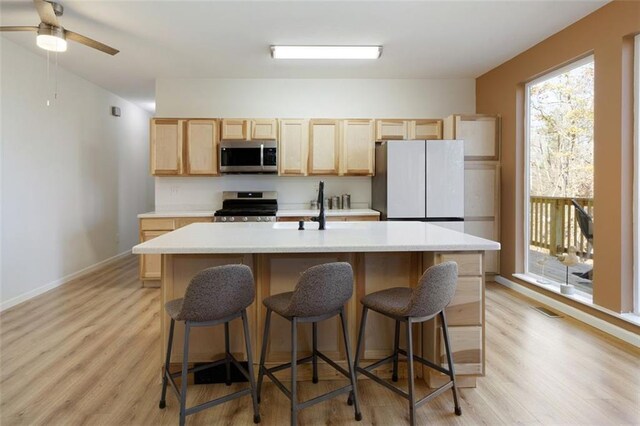 kitchen with ceiling fan, stainless steel appliances, light hardwood / wood-style floors, a kitchen bar, and a kitchen island with sink