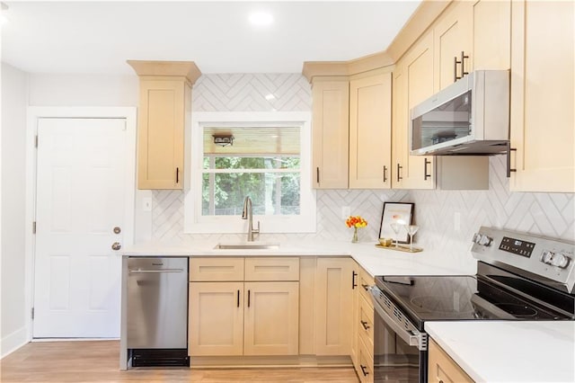 kitchen with appliances with stainless steel finishes, a sink, light wood-style floors, light countertops, and backsplash