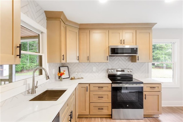 kitchen with light stone counters, a sink, stainless steel appliances, light wood-type flooring, and backsplash