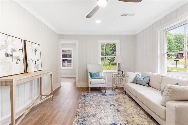 living area featuring crown molding, a ceiling fan, baseboards, wood finished floors, and visible vents