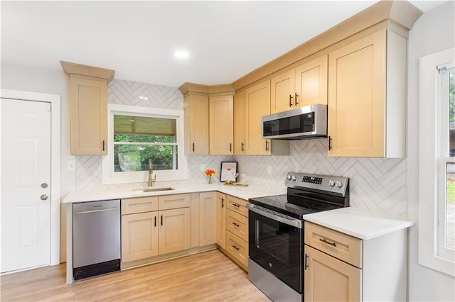 kitchen with light brown cabinetry, light countertops, tasteful backsplash, a sink, and appliances with stainless steel finishes