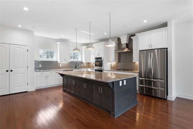 kitchen featuring gas stovetop, freestanding refrigerator, dark wood-type flooring, white cabinetry, and wall chimney range hood