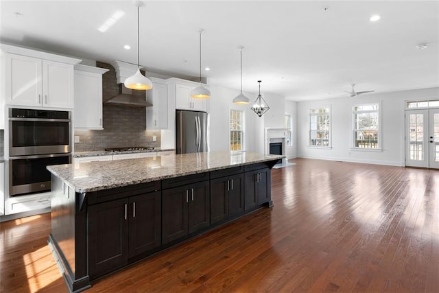 kitchen with dark wood-type flooring, tasteful backsplash, a kitchen island, appliances with stainless steel finishes, and wall chimney range hood