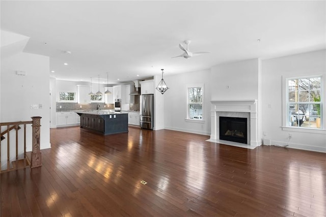 unfurnished living room featuring ceiling fan with notable chandelier, a sink, recessed lighting, a fireplace, and dark wood-style flooring