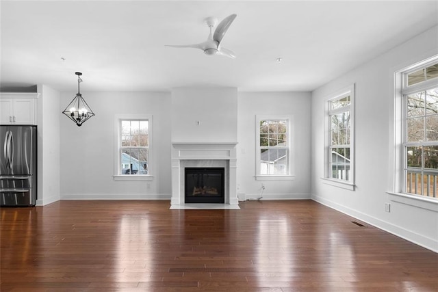 unfurnished living room featuring baseboards, ceiling fan with notable chandelier, dark wood-style flooring, and a premium fireplace