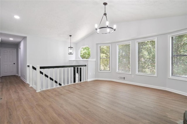 unfurnished room featuring an inviting chandelier, vaulted ceiling, and a wealth of natural light