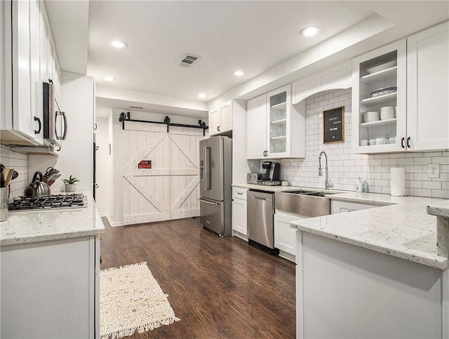 kitchen with white cabinets, a barn door, stainless steel appliances, and light stone counters