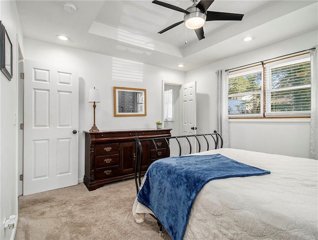 bedroom featuring ceiling fan, a raised ceiling, and light colored carpet