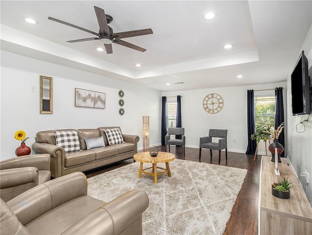 living room with a raised ceiling, ceiling fan, and dark wood-type flooring