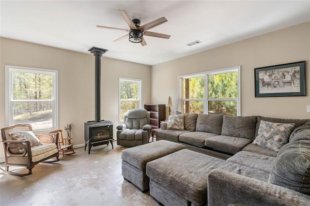 living room featuring a healthy amount of sunlight, ceiling fan, a wood stove, and concrete flooring