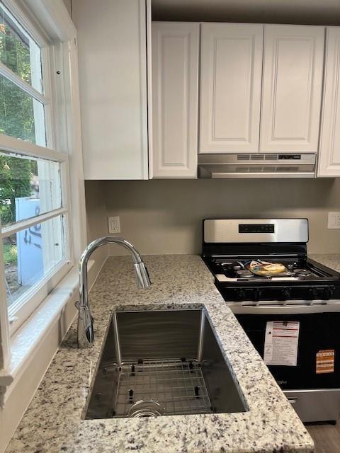 633 Tom Read Dr, Marietta, GA 30062 - kitchen with stainless steel gas range, under cabinet range hood, a sink, white cabinetry, and light stone counters