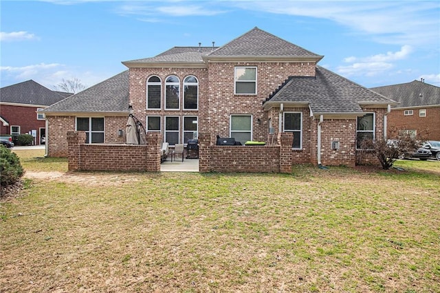 back of property with a shingled roof, a patio area, brick siding, and a lawn