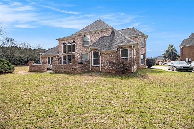 view of front facade with brick siding, roof with shingles, and a front lawn