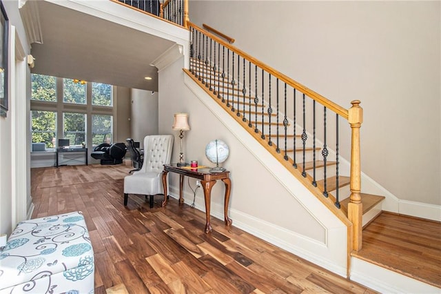 staircase with baseboards, wood finished floors, and a towering ceiling