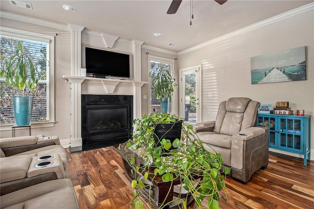 living area featuring visible vents, ceiling fan, a fireplace with flush hearth, ornamental molding, and wood finished floors