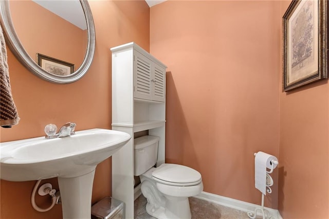 half bath featuring tile patterned floors, baseboards, toilet, and a sink