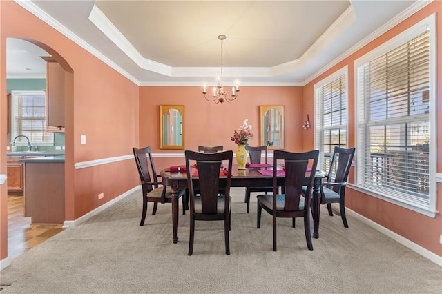 dining space with a tray ceiling, light carpet, arched walkways, and plenty of natural light