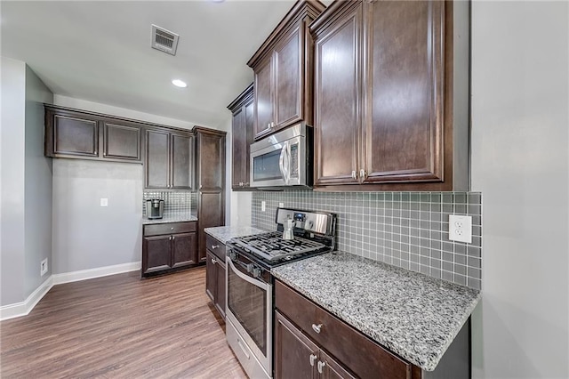 kitchen featuring stainless steel appliances, light stone countertops, dark brown cabinets, and decorative backsplash