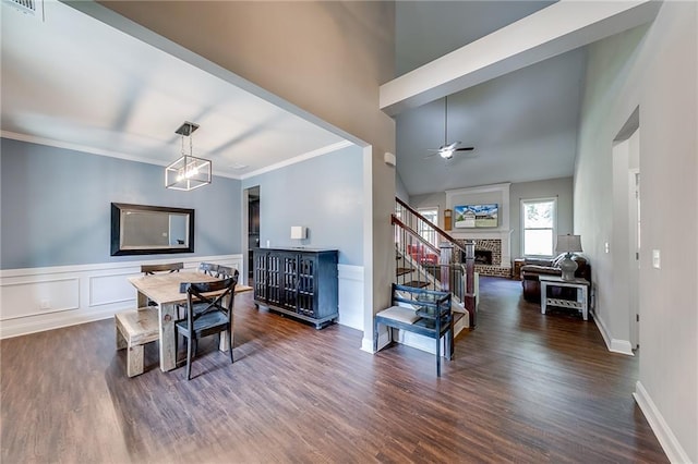 dining area with dark hardwood / wood-style flooring, a brick fireplace, ceiling fan with notable chandelier, and crown molding