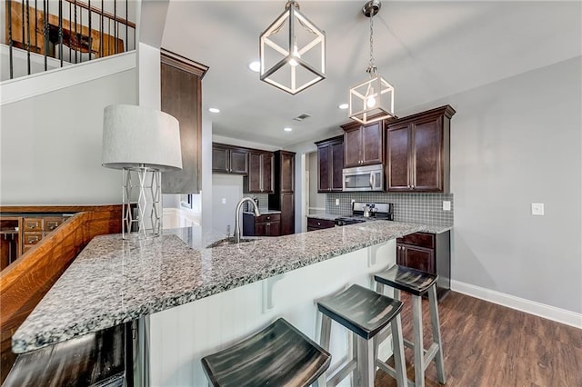 kitchen with dark brown cabinets, appliances with stainless steel finishes, dark hardwood / wood-style flooring, light stone countertops, and backsplash