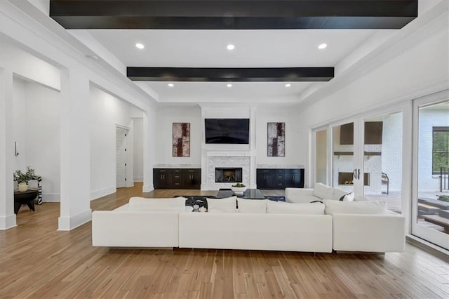 living room with light wood-type flooring, a premium fireplace, and beamed ceiling