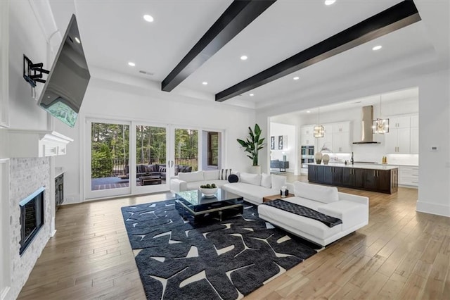 living room featuring beamed ceiling, hardwood / wood-style floors, a chandelier, and a fireplace