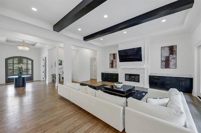 living room featuring beamed ceiling, light hardwood / wood-style floors, and a notable chandelier