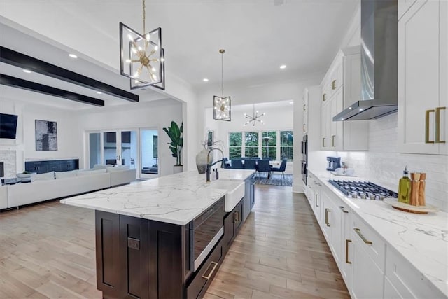 kitchen with a kitchen island with sink, light wood-type flooring, pendant lighting, white cabinetry, and wall chimney exhaust hood