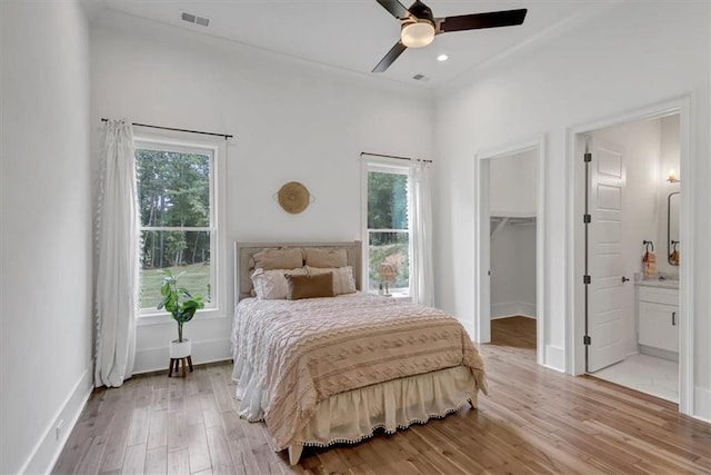 bedroom featuring a walk in closet, a closet, ensuite bathroom, light hardwood / wood-style floors, and ceiling fan