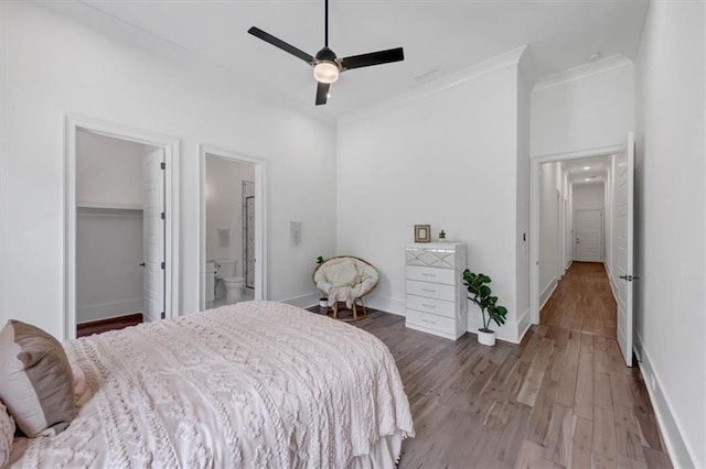 bedroom featuring a walk in closet, connected bathroom, ornamental molding, hardwood / wood-style flooring, and ceiling fan