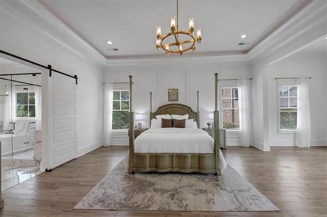 bedroom with a barn door, a raised ceiling, and hardwood / wood-style floors