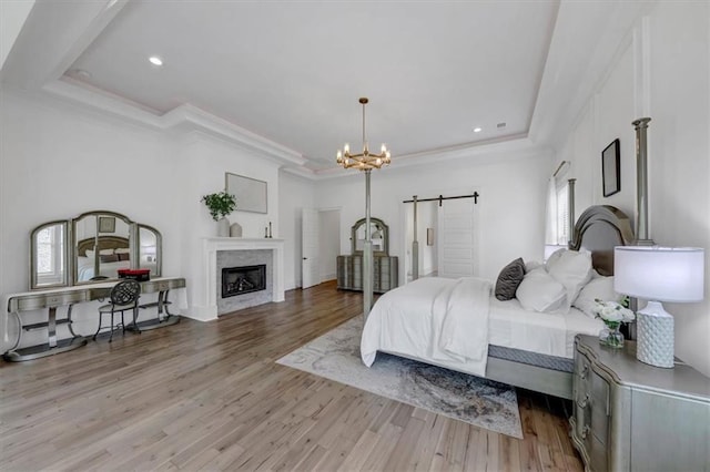 bedroom featuring a barn door, a tray ceiling, a premium fireplace, and light hardwood / wood-style flooring