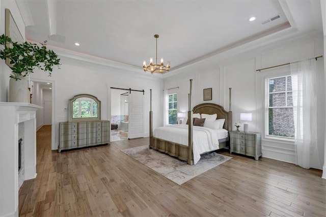 unfurnished bedroom with a barn door, a raised ceiling, and light hardwood / wood-style floors