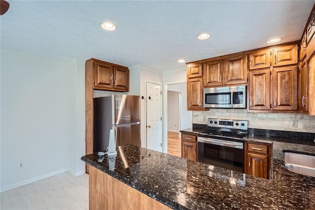 kitchen with dark stone countertops, baseboards, light wood-style floors, appliances with stainless steel finishes, and backsplash