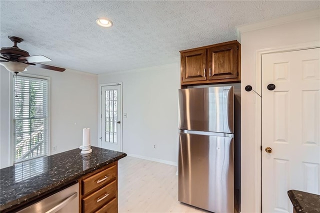 kitchen featuring a ceiling fan, dark stone counters, light wood-style flooring, stainless steel appliances, and a textured ceiling