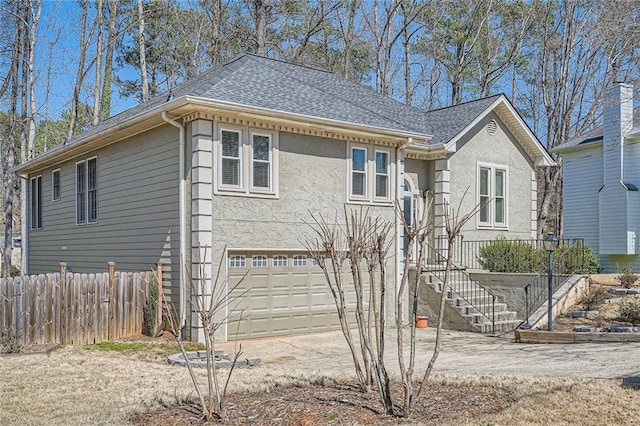 exterior space with fence, concrete driveway, an attached garage, a shingled roof, and stairs