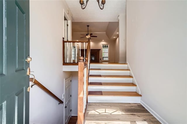 stairway with wood finished floors, ceiling fan with notable chandelier, and baseboards