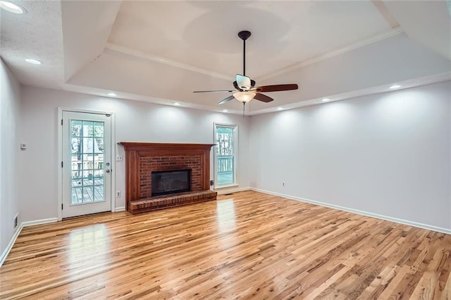 unfurnished living room featuring light wood-type flooring, a ceiling fan, recessed lighting, a raised ceiling, and a brick fireplace