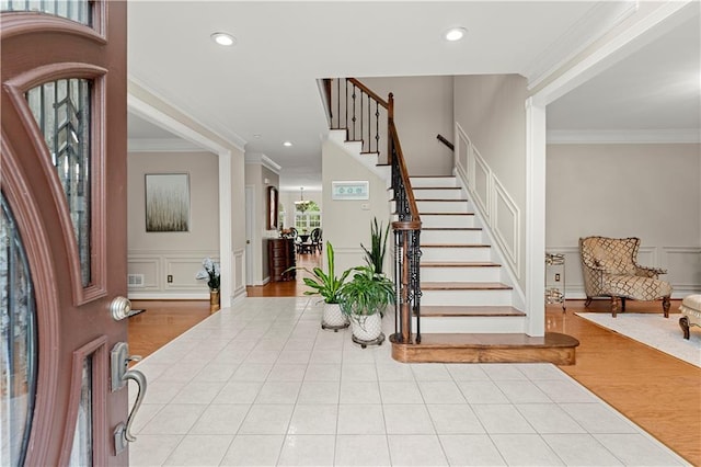 foyer entrance with ornamental molding, wood finished floors, a decorative wall, and stairs