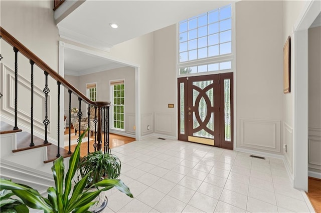 entryway with light tile patterned floors, a decorative wall, stairs, ornamental molding, and wainscoting